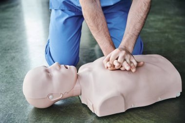 cropped view of professional healthcare worker doing chest compressions on CPR manikin, cardiopulmonary resuscitation, life-saving skills and emergency preparedness concept clipart