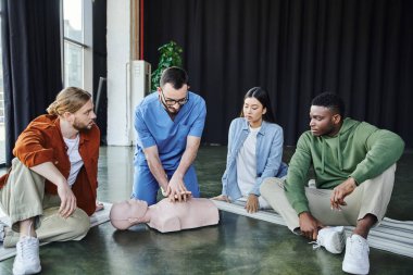 İlk yardım semineri sırasında genç çoklu kültür ekibine kardiyopulmoner resüsitasyon tekniklerini gösterirken kalp masajı manikini yapan uzman sağlık görevlileri