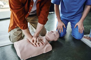 partial view of young man doing chest compressions on CPR manikin during first aid seminar near professional paramedic, cardiopulmonary resuscitation, life-saving skills and techniques concept clipart