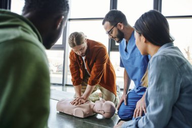 cardiopulmonary resuscitation, young man doing chest compressions on CPR manikin during hands-on learning on first aid training seminar near medical instructor and multiethnic participants clipart