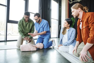 Tıbbi eğitmen Afro-Amerikan erkek kardiyopulmoner resüsitasyon tekniklerini açıklarken suni teneffüs manikini ve genç çoklu etnik ekip, hayat kurtarma becerileri ve acil durum hazırlık konsepti