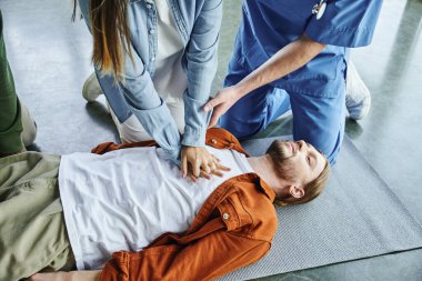 Kardiyopulmoner resüsitasyon, profesyonel eğitmen kadının eğitim odasında yatan genç adama göğüs kompresyonu uygulamasına yardım etmesi, etkili hayat kurtarma becerileri ve teknikler konsepti