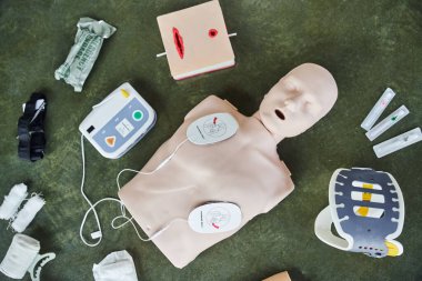 top view of CPR manikin, automated external defibrillator, wound care simulator, neck brace, bandages, syringes and compression tourniquet, medical equipment for first aid training clipart