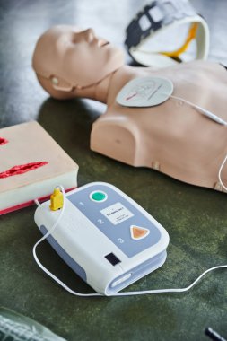 Otomatik dış defibrilatör, yara bakım simülatörü, kalp masajı manikürü ve boyun desteği, eğitim odasındaki bulanık arka plan, ilk yardım eğitimi için tıbbi ekipmanlar. 