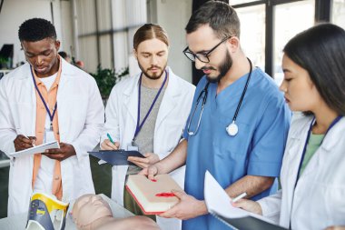 İlk yardım semineri sırasında beyaz önlüklü çeşitli ırklar arası öğrencilere yara bakımı simülatörü gösteren profesyonel sağlık görevlisi, acil durum tepki kavramı