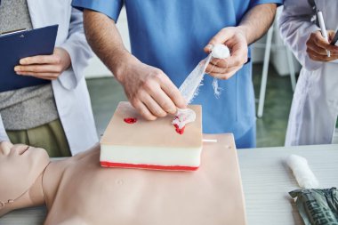 Simülatördeki tıbbî eğitmen tampon yarasının kırpılmış görüntüsü suni teneffüs manikürü ve eğitim odasında öğrenciler, ilk yardım semineri, sağlık hizmetleri ve acil durum hazırlık konsepti.