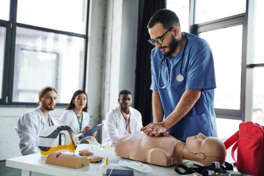 Beyaz önlüklü genç çok kültürlü öğrenciler ilk yardım semineri sırasında kalp masajı yapan tıp hocalarına bakıyor, hayat kurtarma becerileri ediniyor ve pratik yapıyor.