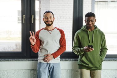 Modern ofisteki kameraya bakarak şık giyinen, ırkçı iş arkadaşları. Afro-amerikan cep telefonuyla zafer işareti gösteren neşeli sakallı adam.
