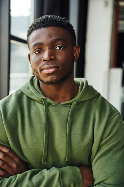 自信而时尚的非洲裔美国人 在当代办公场所看着相机 绿色时髦的帽衫 双臂交叉 年轻而成功的企业家 — 图库照片