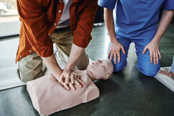 partial view of young man doing chest compressions on CPR manikin during first aid seminar near professional paramedic, cardiopulmonary resuscitation, life-saving skills and techniques concept