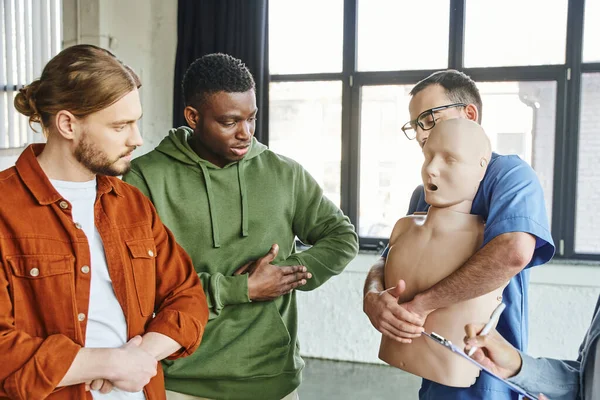stock image multiethnic participants of medical seminar looking at healthcare worker with CPR manikin showing first aid techniques in case of choking, emergency situations preparedness concept