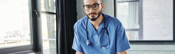 救急セミナー前の研修室でカメラを見る眼鏡と青の制服を着た重大で髭のある医療従事者救命スキル開発コンセプトバナー — ストック写真