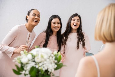 wedding preparations, cheerful multicultural bridesmaids with champagne looking at bride on grey background, admire her style, fitting, bridesmaid gowns, diversity, blurred  clipart