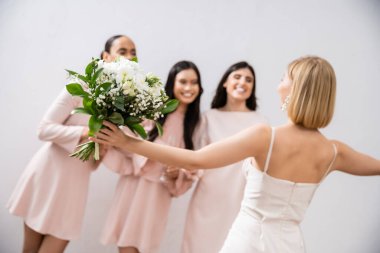 wedding preparations, cheerful bride with bouquet standing near blurred multicultural bridesmaids on grey background, dress fitting, bridesmaid gowns, wedding dress, diversity  clipart
