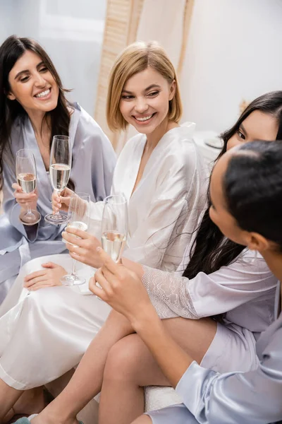 stock image bridal party, interracial girlfriends holding glasses with champagne, celebration before wedding, brunette and blonde women, happy bride and bridesmaids, diverse ethnicities, positivity, bedroom 