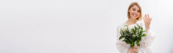 happiness, joyful bride with blonde hair standing in white silk robe and holding bridal bouquet, showing engagement ring, young woman, beautiful, excitement, feminine, white flowers, banner 