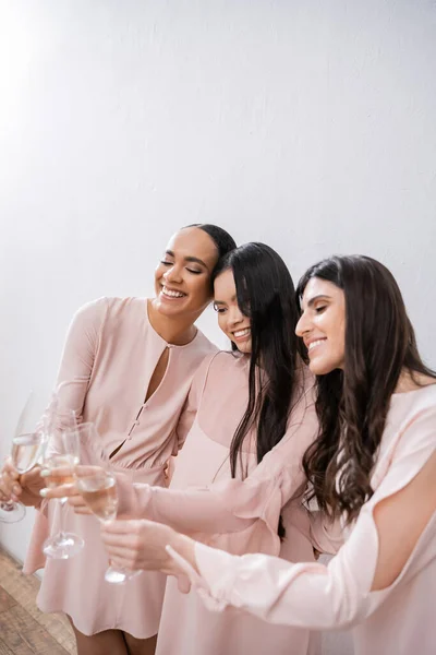 三位多文化的伴娘 穿着淡淡的粉红连衣裙的漂亮女人 在灰色背景 多样性 欢呼声和不同种族的背景下 叮咬着几杯香槟 — 图库照片