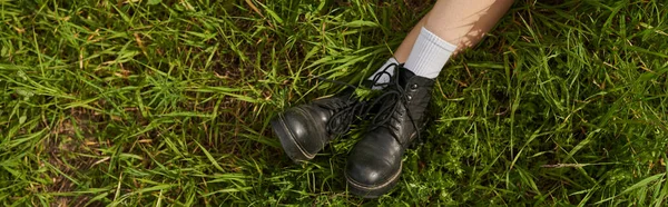 スタイリッシュなブーツで女性の足のトップビューは 芝生の牧草地の屋外に座って 自然の風景 — ストック写真