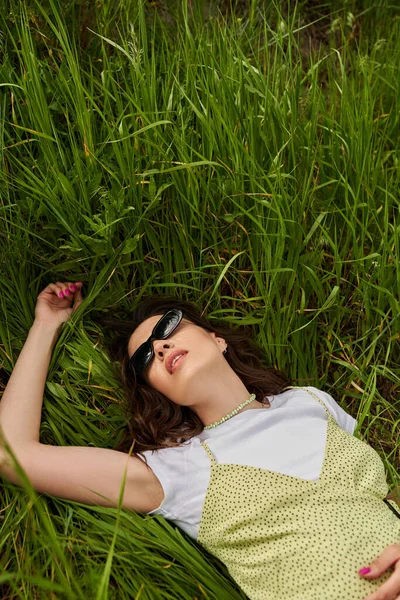 穿着太阳镜和太阳衣 躺在田野绿草上的时髦黑发女人的头像 自然景观 休闲的自然景观 乡村风景 — 图库照片