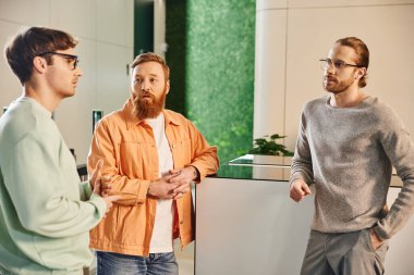 Düşünceli sakallı adam şık giyinmiş ciddi iş ortaklarına bakıyor modern ofis alanındaki iş projelerini tartışıyor beyin fırtınası yapıyor, başlangıç planlaması yapıyor, problem çözüyorlar.