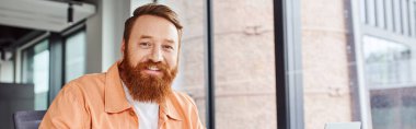 professional headshot of happy, charismatic and bearded businessman smiling at camera in contemporary office environment, portrait, business success concept, banner with copy space clipart