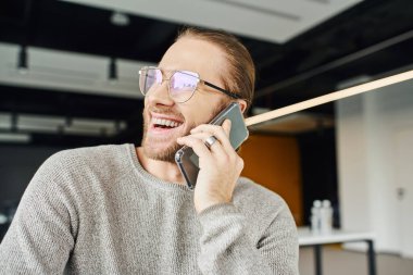Modern ofis, iş verimliliği ve başarı konseptinde cep telefonuyla yapılan konuşmada şık gözlüklü, sıradan kıyafetleri olan ve gülen heyecanlı girişimci.