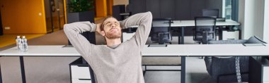 Modern ofis ortamında iş yerinde dinlenirken kapalı gözlerle ve ellerle rahat rahat oturan şık gözlükler ve günlük giysiler içindeki yorgun işadamı.