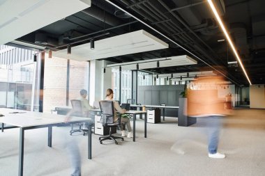 long exposure of businessman walking near colleagues working in spacious coworking environment of contemporary office, dynamic business and productivity concept clipart