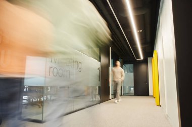 Çağdaş ofiste, çalışma ortamının koridorunda bulanık toplantı odasında yürüyen enerjik iş adamının uzun pozu, dinamik iş konsepti