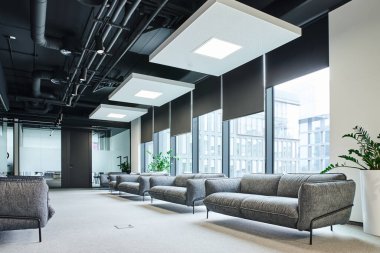 Gri ve rahat koltukları olan geniş bekleme salonu, yeşil doğal bitkiler ve modern çalışma odasındaki büyük pencereler, çalışma alanı organizasyonu konsepti