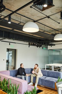 Yeşil santrallerin yanındaki yumuşak koltukta oturan ve modern iş yeri, ortaklık ve başarı konseptinin dinlenme odasında proje planlayan şık gündelik kıyafetler giyen iş ortakları.