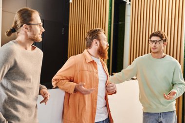 Çağdaş çalışma ortamı ve iş ortaklığı lobisinde yeni bir proje planlarken gözlüklü ve günlük kıyafetlerle ciddi iş arkadaşlarıyla konuşan sakallı iş adamı