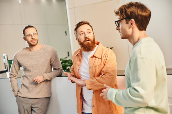 вдумчивый бородатый предприниматель смотрит на коллег, обсуждающих возможность запуска проекта в зале современного офисного пространства, коворкинга и сотрудничества, концепцию успеха бизнеса