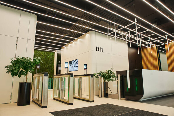 entrance of office center, spacious lobby, high tech interior, entrance turnstiles, reception desk, green natural plants, led lighting, workspace organization concept