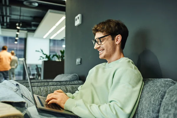 Vidám Üzletember Alkalmi Ruhákban Stílusos Szemüvegben Gépelés Laptopon Miközben Kényelmes — Stock Fotó