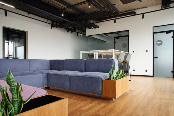 зона ожидания, гостиная в современном офисе с удобным диваном, высокий стол и стулья, зеленые природные растения, высокотехнологичный стиль интерьера, концепция организации рабочего пространства