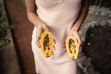 Bahçe merkezinde dikilen, elinde taze kesilmiş papaya tutan, moda düşkünü, tropikal bitkilerden esinlenen, yaz konseptinden esinlenilmiş genç Afrikalı Amerikalı kadın manzarası.