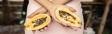 Bahçe merkezinde dikilirken papaya kesilen yaz elbisesi giyen Afro-Amerikan genç kadın manzarası, tropikal sarhoşluk, afiş, yaz konsepti ile çevrili moda kadın. 