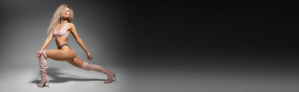 full length of fashion-forward and sexy woman in lace lingerie and long boots standing in expressive pose on black and grey background, toned body, wavy ash blonde hair, banner with copy space