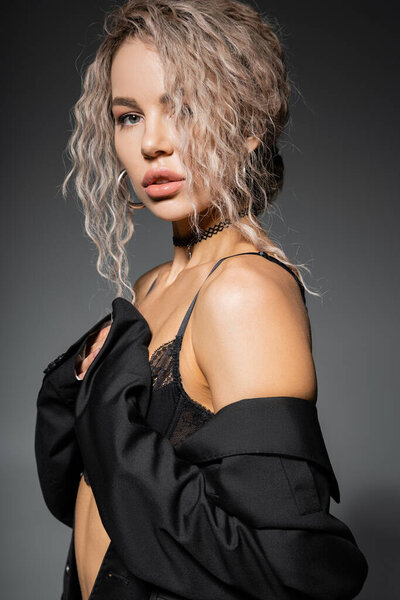 портрет сексуальной модной женщины в кружевном бюстгальтере и трусиках, позирующей и смотрящей на камеру на сером фоне, окрашенной золой блондинки, выразительным взглядом, женственностью и современным стилем