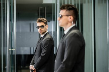 Koruma servisi, otel güvenliği, takım elbiseli yakışıklı adam ve güneş gözlüğü lobide duruyor iş ortağı, tetikte, koruma ve iş, profesyonel vesikalıklar, kameraya bakıyor.  