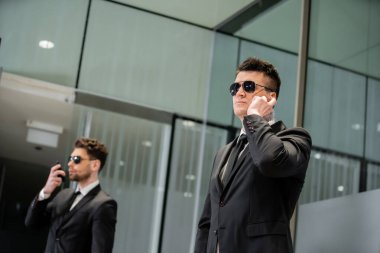 hotel security concept, professional guards in suits and sunglasses standing in hotel lobby, handsome man with earpiece communicating with work partner, luxury hotel, vigilance, private bodyguards clipart