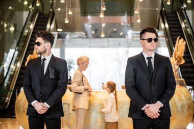 personal security, handsome bodyguards in suits and sunglasses protecting mother and child in hotel lobby, rich and luxury lifestyle, woman and girl standing at reception desk clipart