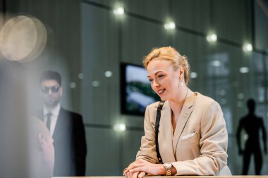Otelde resepsiyonistle, konukseverlik sektöründe konuşan cesur bir kadın, otel personeliyle iletişim kuran sarışın ve neşeli bir iş kadını, kişisel güvenlik, özel güvenlik, arka planda korumalar. 