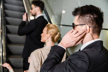 Kişisel güvenlik kavramı, müşterilerin güvenliğini korurken iletişim kuran profesyonel korumalar, zengin yaşam tarzı, sarışın ve başarılı kadın ve otelin yürüyen merdivenlerinde duran küçük kız.