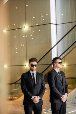 security management of hotel, two handsome men in formal wear and sunglasses, bodyguards on duty, safety measures, vigilance, suits and ties, private security, strong guards, luxury living  clipart