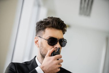 surveillance, bodyguard communicating through walkie talkie, man in sunglasses and black suit with tie, hotel security, safety management, uniformed guard on duty, professional headshots  clipart