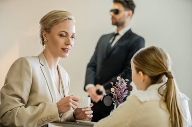 Sarışın bir kadın elinde kahve fincanıyla arka planda bulanık koruma, güvenlik servisi, özel güvenlik konsepti, anne ve çocuğun kaliteli zaman geçirme konusunda reşit olmayan kızıyla konuşuyor. 