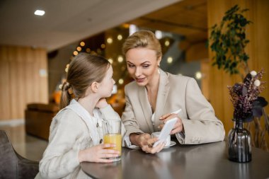 Sarışın anne ve kız birlikte kaliteli zaman geçiriyorlar, kızının yanında akıllı telefon tutan kadın, alet kullanıyor, çalışan ebeveyn ve çocuk, modern ebeveynlik, aile bağı 