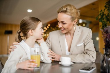 Mutlu anne kızıyla kaliteli zaman geçiriyor, sarışın kadın içki ve akıllı telefonun yanında reşit olmayan kızı kucaklıyor, çalışan ebeveyn ve çocuk, modern ebeveynlik, aile bağı 